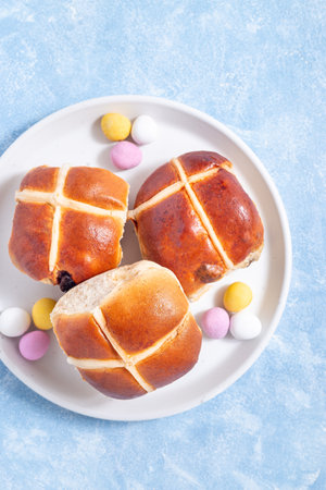 Hot cross buns on white plate with chocolate candy eggs. Traditional easter food, vertical, top viewの写真素材