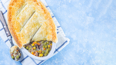 Beef pot pie or deep dish pie in baking dish, crust broken open, horizontal, top view, copy space