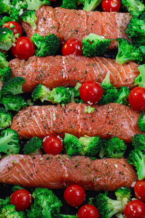 Ready to bake raw salmon fillet with broccoli and tomato on frying tray, vertical, top view, closeup
