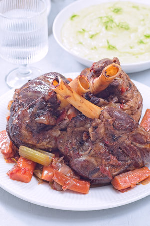 Braised lamb shanks with vegetables on a white plate, vertical closeupの写真素材