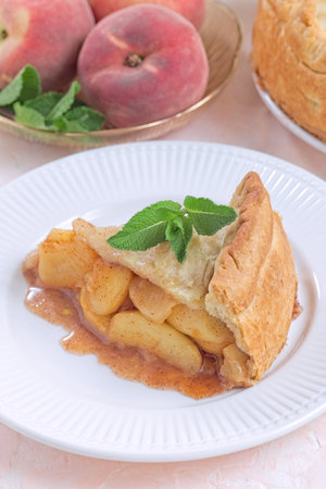Old fashioned deep dish peach pie slice garnished with fresh mint, on white plate, verticalの写真素材