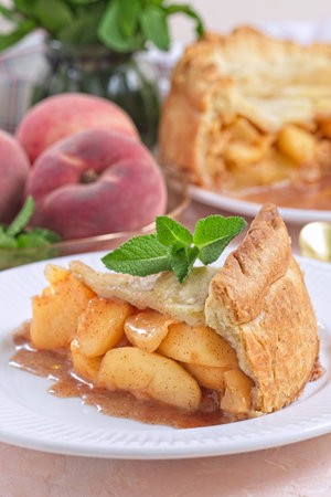 Delicious peach pie slice garnished with fresh mint, on white plate, verticalの写真素材