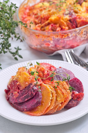Sweet potato, parsnips and beet root au gratin with thyme and melted cheese, on plate, verticalの写真素材