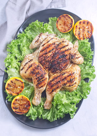 Spatchcocked grilled chicken with lemon garlic marinade on lettuce with lemon, vertical top viewの写真素材