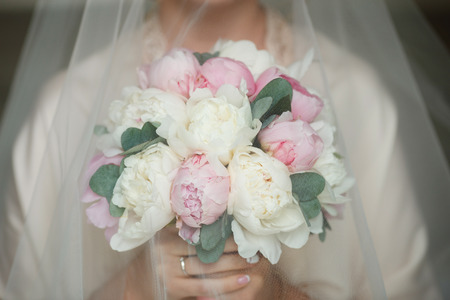 Charming and delicate bride holding bouquet with peonies and eucalyptus. Pink and white peonies under the veil of the brideの写真素材