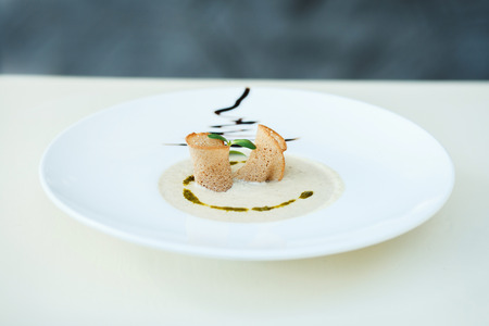 bowl of vegetarian mushroom puree soup in a large plate on bokeh background of greens