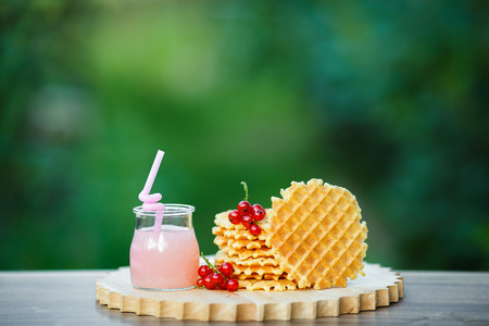 Belgian waffles with fresh berries on cutting board on background of green bokeh. grapefruit juice. pink cocktail with a straw.の写真素材