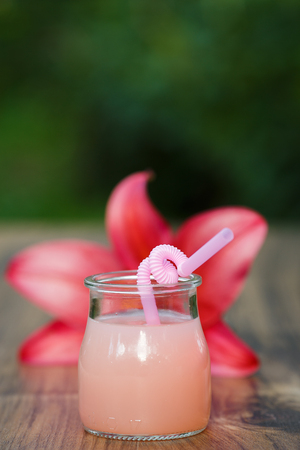 jar of cold pink cocktail with straw on green background bokehの写真素材