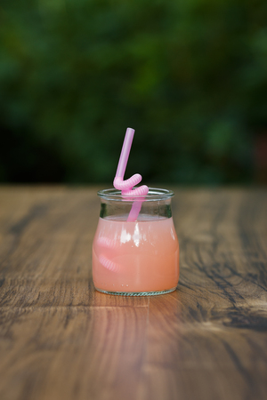 jar of cold pink cocktail with straw on green background bokehの写真素材