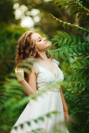 Outdoors portrait of beautiful young caucasian woman in dress over green foliage on background. Green gardenの写真素材