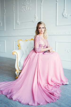 godlike blonde girl in pink wedding dress sitting in the chair in classic white interior.の写真素材