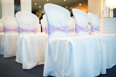 chairs decorated with white cloth with purple bows for wedding guestsの写真素材