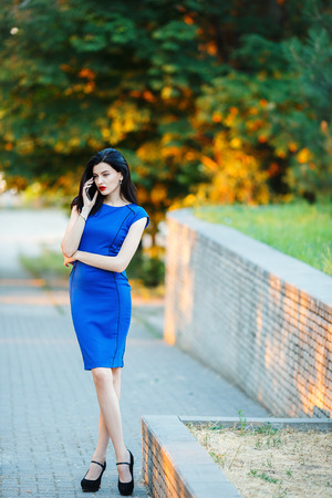 Attractive businesswoman in blue short dress. She wears high heels, speaking on phoneの写真素材