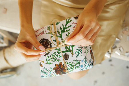 Young woman in gold dress hands a new year's gift wrapped in paper. Christmas cute present.の写真素材