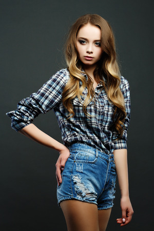 Young blonde model with long flowing hair. Dressed in stylish american clothes. Shorts and checkered shirt Studio.の写真素材