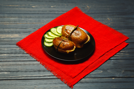 Delicious baked potatoes with garlic in black rustic plate. Pickled cucumbers behind. Country-style roasted potatoesの写真素材