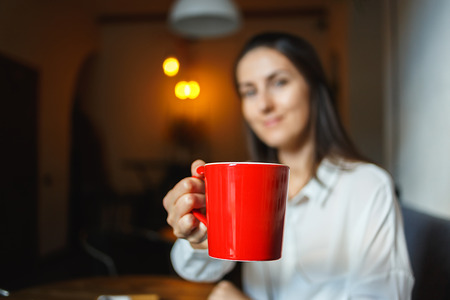 Red cup of coffee in the hands of a beautiful smiling girlの写真素材