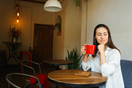Beautiful smiling woman holding red coffee cup. Young model in cafeの写真素材