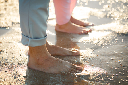 Legs on beach. Foot spa. A young loving couple hugging and kissing on the beach at sunset. Two lovers, man and woman barefoot near the water. Summer in loveの写真素材