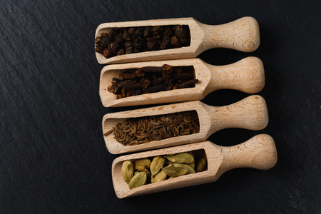 Various of spices and herbs in wooden spoons. Flat lay of spices on black stoneの写真素材