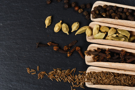 Various of spices and herbs in wooden spoons. Flat lay of spices on black stoneの写真素材