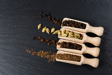 Various of spices and herbs in wooden spoons. Flat lay of spices on black stoneの写真素材