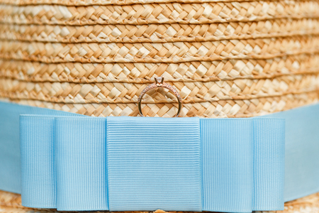 Golden engagement ring with diamonds lying on the french straw hat with blue ribbon. Wedding ring offer.の写真素材
