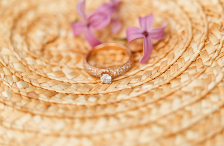 Elegant Golden engagement ring with brilliant and spring natural flowers of lilac on a straw hatの写真素材
