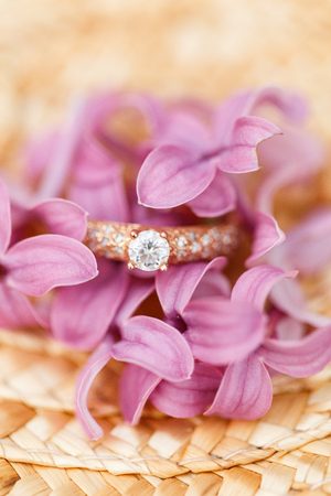 Elegant Golden engagement ring with brilliant and spring natural flowers of lilac on a straw hatの写真素材