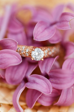 Elegant Golden engagement ring with brilliant and spring natural flowers of lilac on a straw hatの写真素材