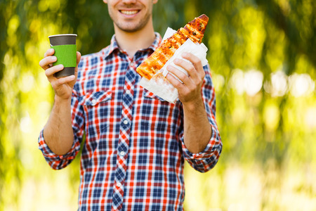Portrait of a young man eating pizza, coffee in his hand. Mockup for products presentations, logo and text. Lifestyle.の写真素材