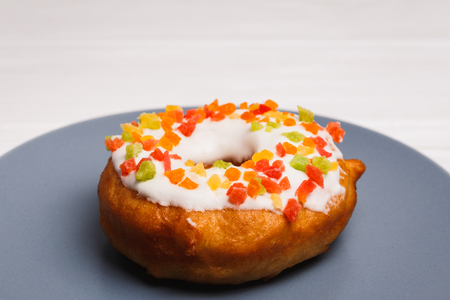 donut in sugar glaze with candied fruits on a blue plateの写真素材