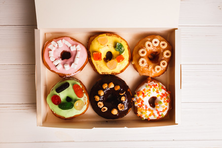 Colored delicious donuts in a box on a white wooden background