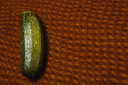Raw green vegetable marrow on brown textile background. Healthy raw food, top view, flat lay.の写真素材