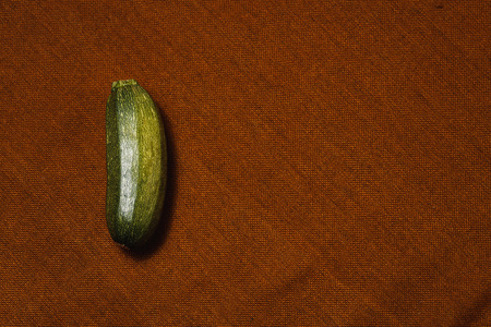 Raw green vegetable marrow on brown textile background. Healthy raw food, top view, flat lay.の写真素材