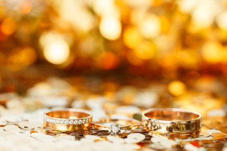 three golden wedding rings with golden bokeh backgroundの写真素材