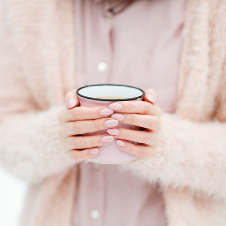 Pink cup of coffee in the hands of a cute girl who freezes in the winter forest. Stylish stock mock upの写真素材