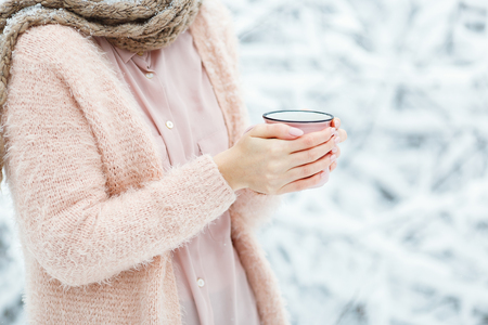 Pink cup of coffee in the hands of a cute girl who freezes in the winter forest. Stylish stock mock upの写真素材