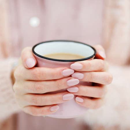 Pink cup of coffee in the hands of a cute girl who freezes in the winter forest. Stylish stock mock upの写真素材