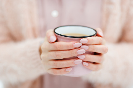 Pink cup of coffee in the hands of a cute girl who freezes in the winter forest. Stylish stock mock upの写真素材