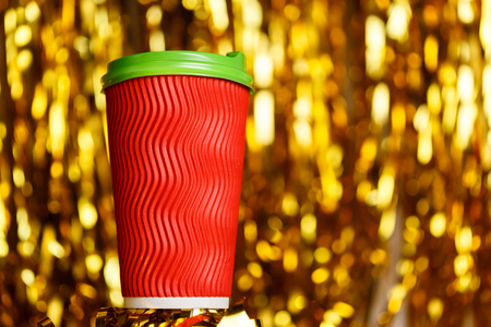 Christmas red cardboard cup of coffee on background with golden metafanの写真素材