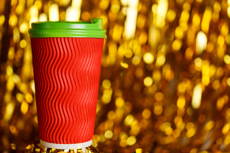 Christmas red cardboard cup of coffee on background with golden metafanの写真素材