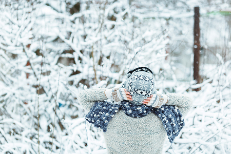 Beautiful girl wearing a gray sweater, hat and scarf under the falling snow in the winter forestの写真素材