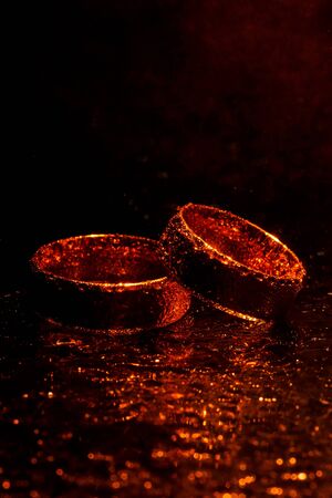Wedding rings with water drops on a dark orange backlight background.の写真素材
