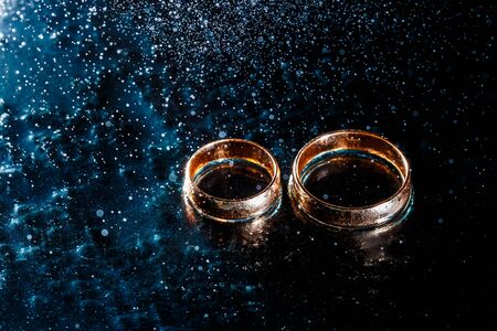 Beautiful wedding golden rings on dark wet glass.の写真素材