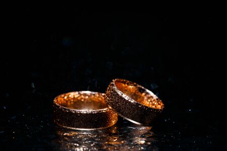 Beautiful wedding golden rings on dark wet glass.の写真素材