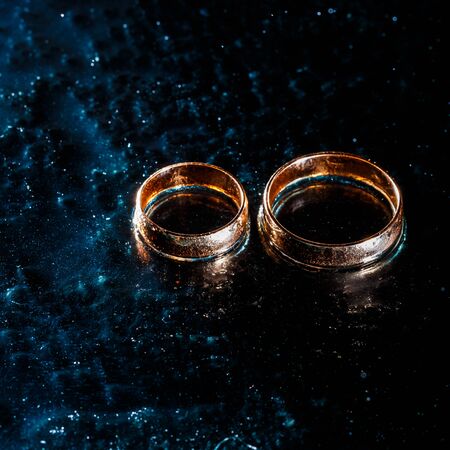 Beautiful wedding golden rings on dark wet glass.の写真素材