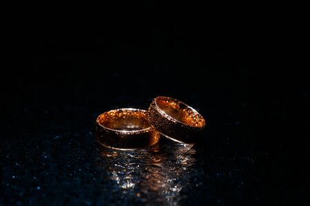 Beautiful wedding golden rings on dark wet glass.の写真素材