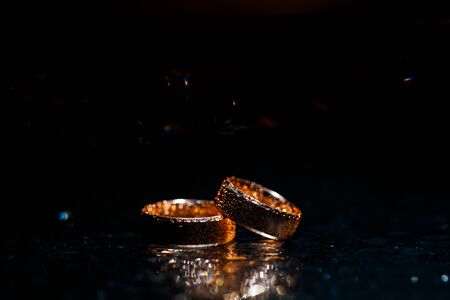 Beautiful wedding golden rings on dark wet glass.の写真素材