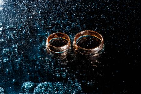Beautiful wedding golden rings on dark wet glass.の写真素材